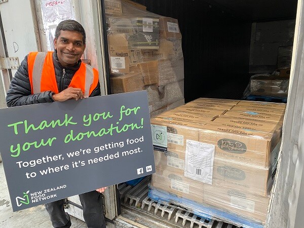 NZFN staff member holding a 'thank you' sign next to a pallet of donated food.