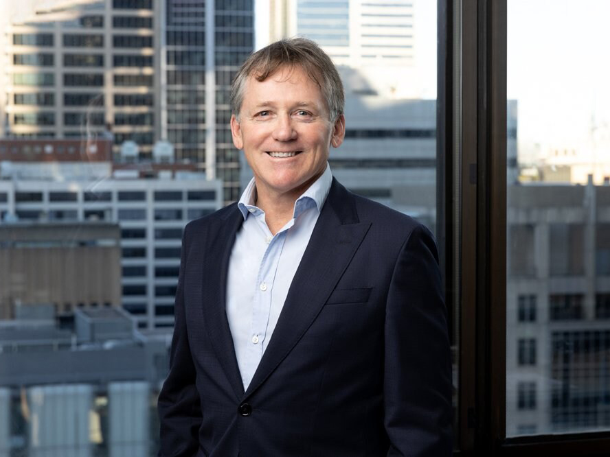 NZFN Board Chairman, David Kirk, standing in front of a window with a city backdrop.