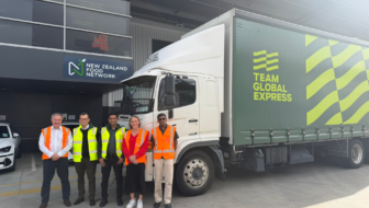 Food distribution in NZFN logistics partnership with Team Global Express. A group standing beside a Team Global Express delivery truck outside a New Zealand Food Network building.