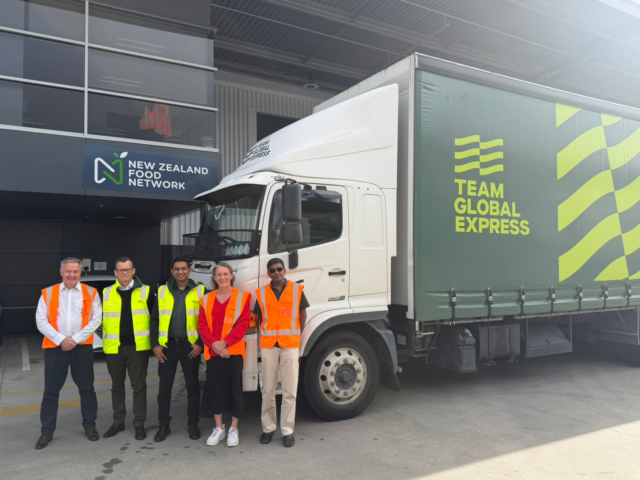 Food distribution in NZFN logistics partnership with Team Global Express. A group standing beside a Team Global Express delivery truck outside a New Zealand Food Network building.
