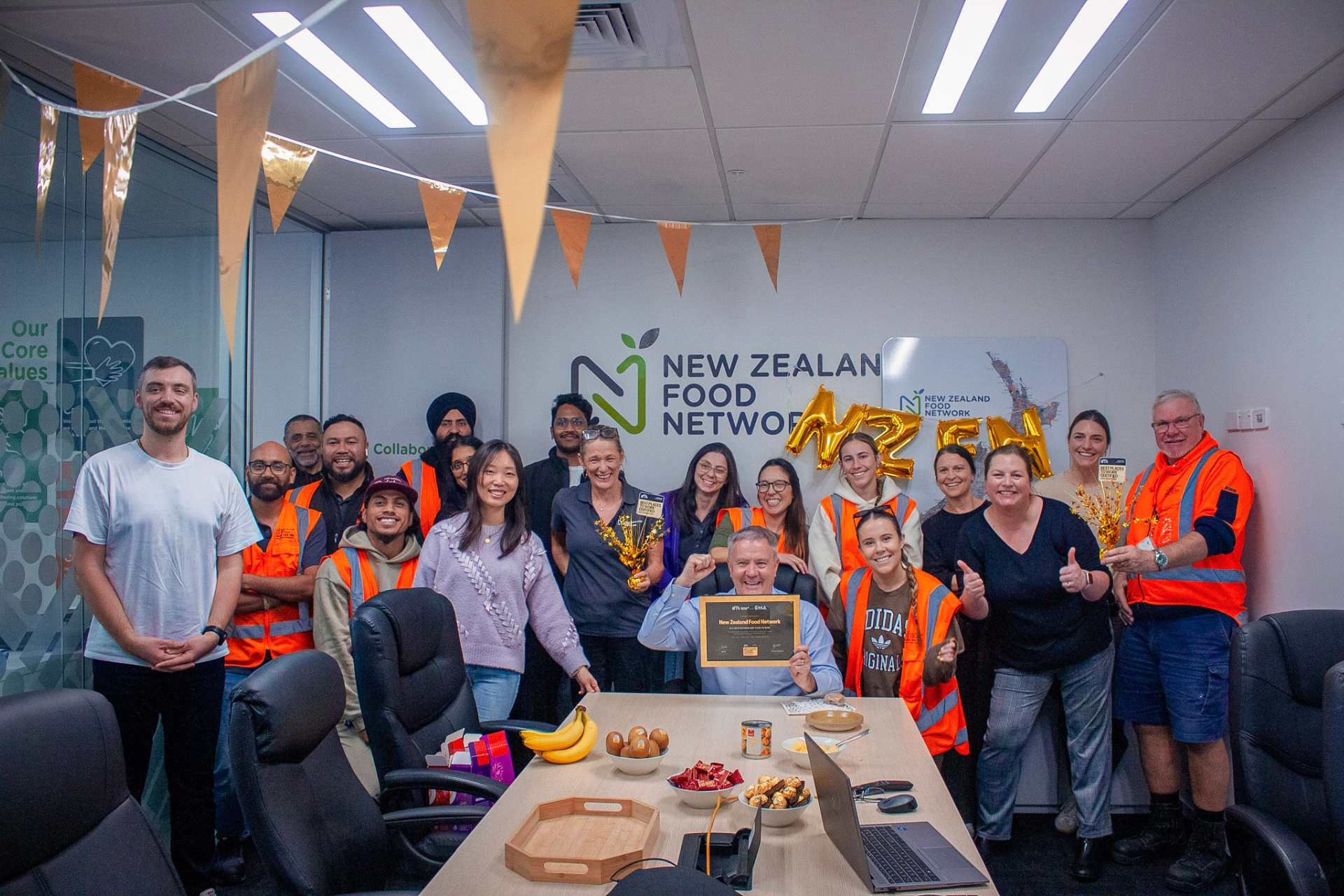 NZFN staff celebrating Best Places to Work Gold certification in office with certificate, decorations and team gathered.