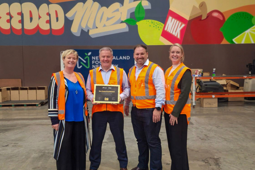 NZFN x BPTW 03 NZFN team wearing high-vis vests holding Best Places to Work Gold certification inside warehouse facility.